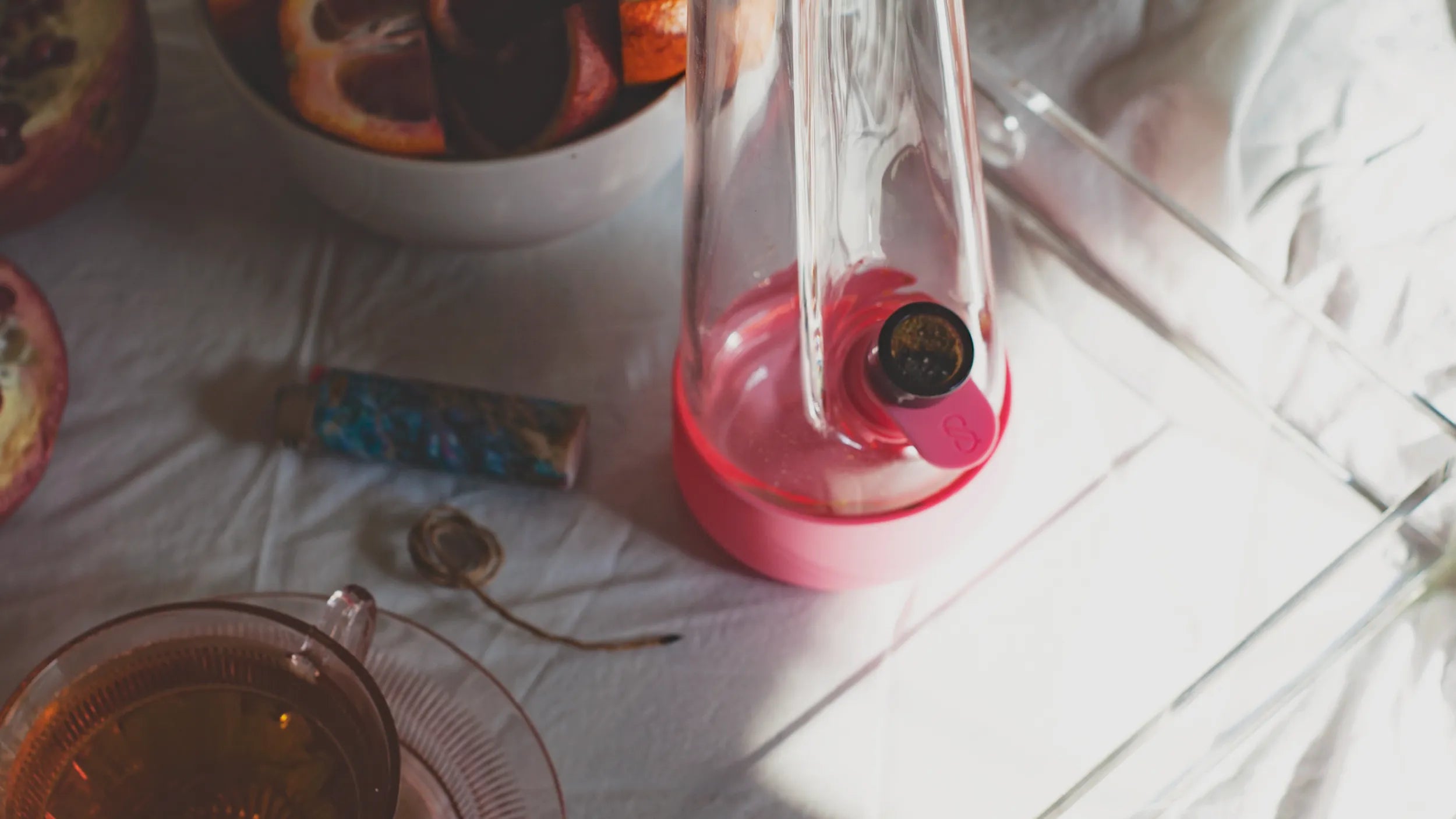 elegant glass bong in pink on a tray with blood orange fruit on a white sheet bed, a wake and bake relaxation moment