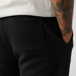 Person wearing black pants with a tattooed arm visible