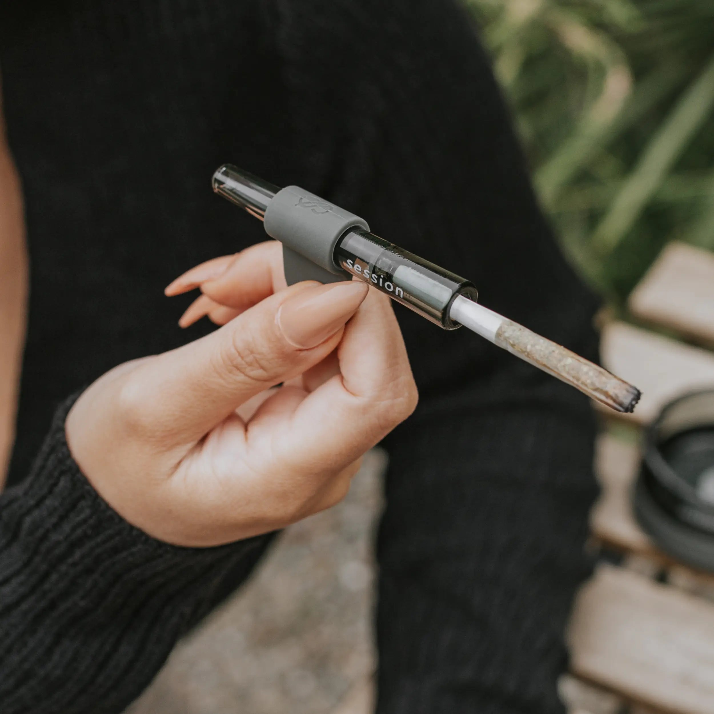 closeup of a female model holding a session goods one hitter in charcoal with a joint attached to it