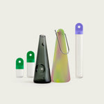Glow-in-the-dark silicone smoking accessory next to a dark glass component, photographed in studio bundled with a stash kit in desire green and moonlight purple