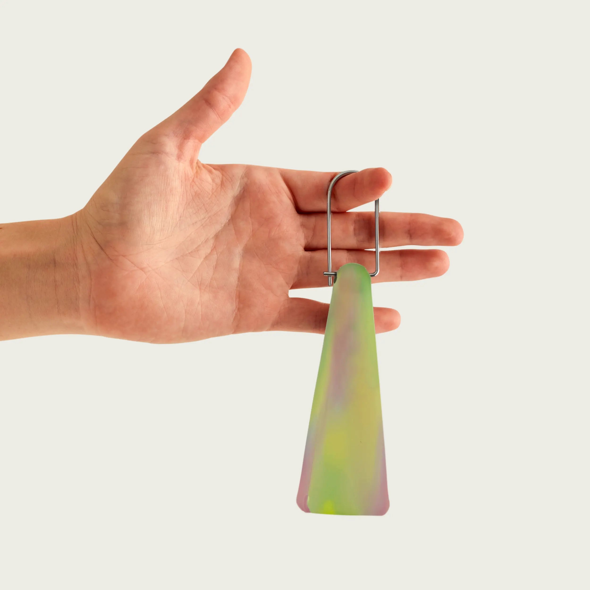 Hand holding Session Goods Aura Green Pipe Sleeve – a colorful, conical silicone accessory with sleek metal clip for secure portability