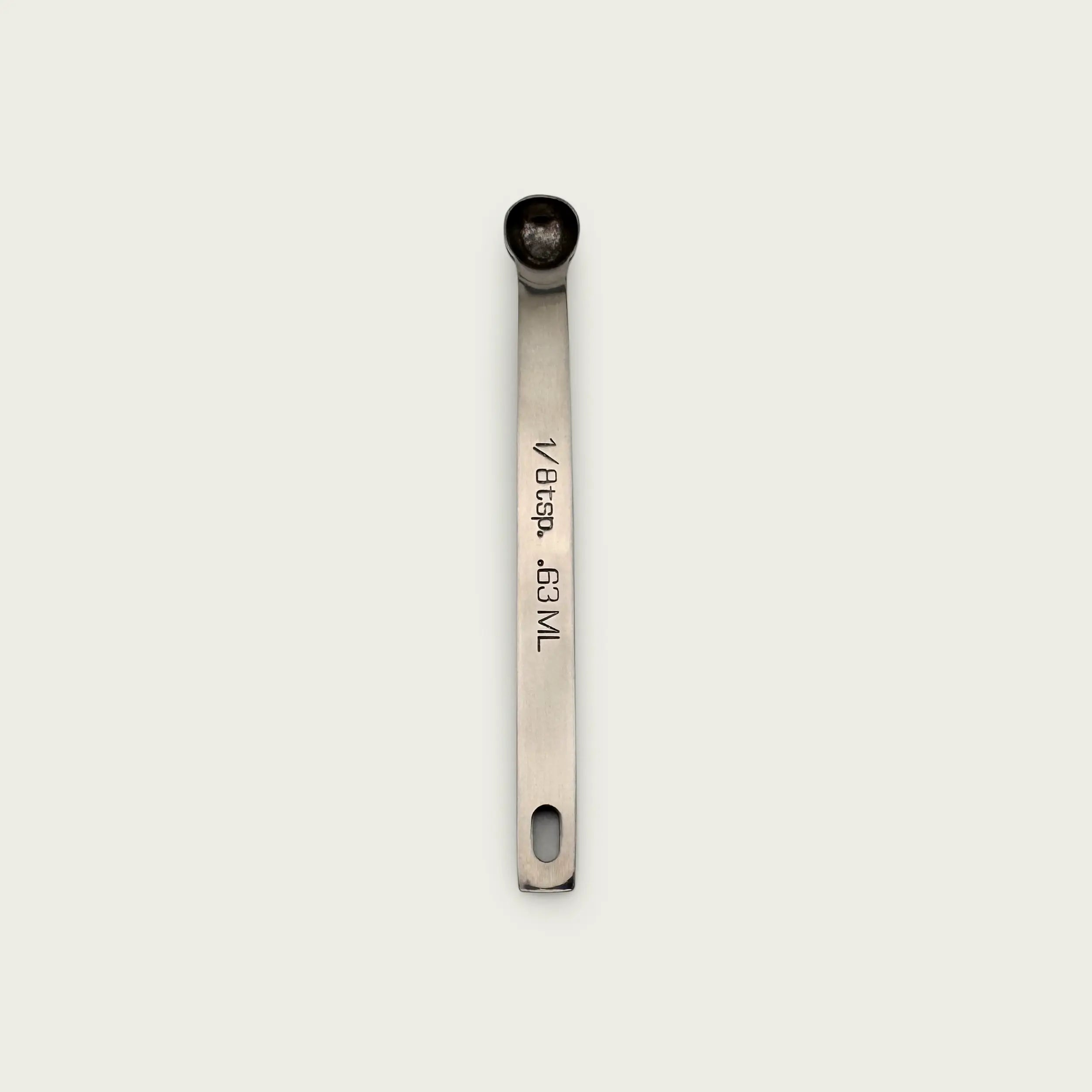Stainless steel 1/8 teaspoon measuring spoon with engraved measurement markings, photographed from above on a light background.