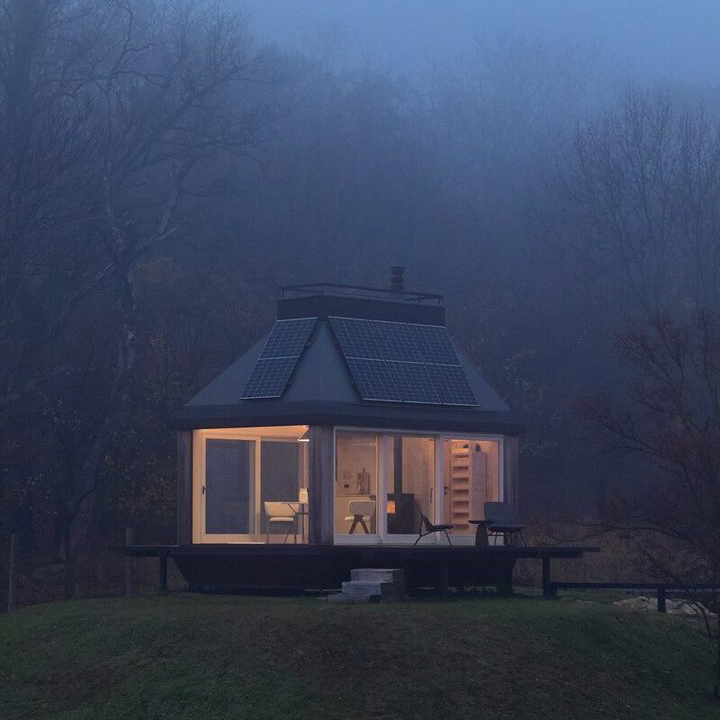 Modern glass cabin surrounded by fog at dusk