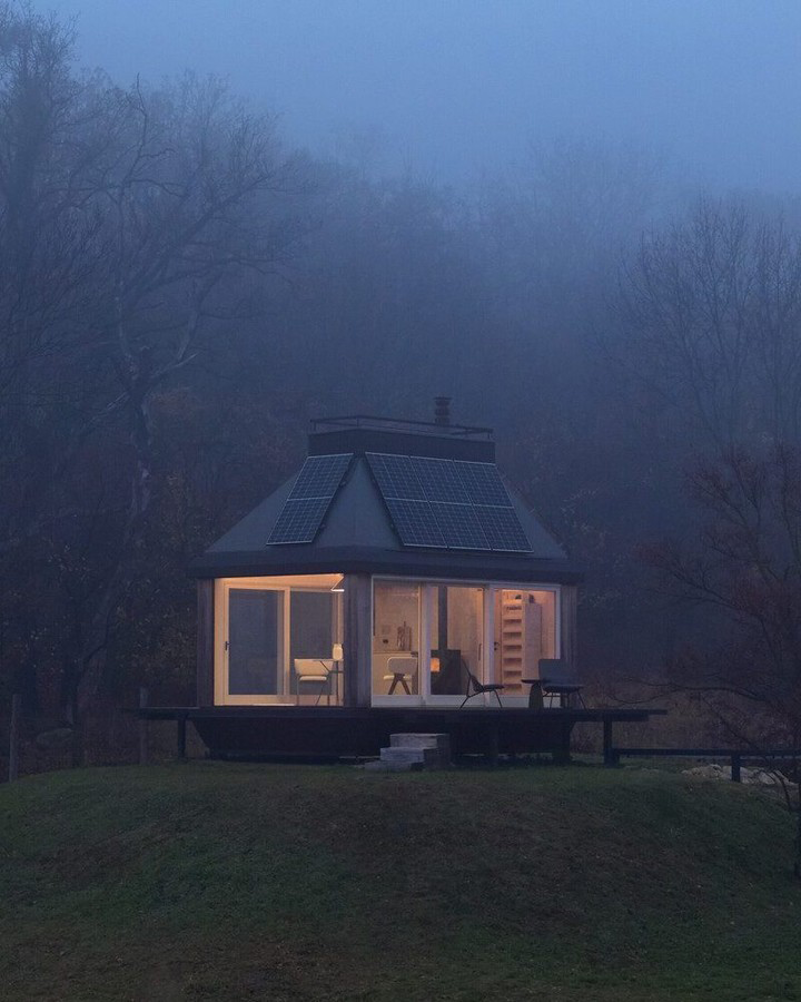Modern glass cabin surrounded by fog at dusk
