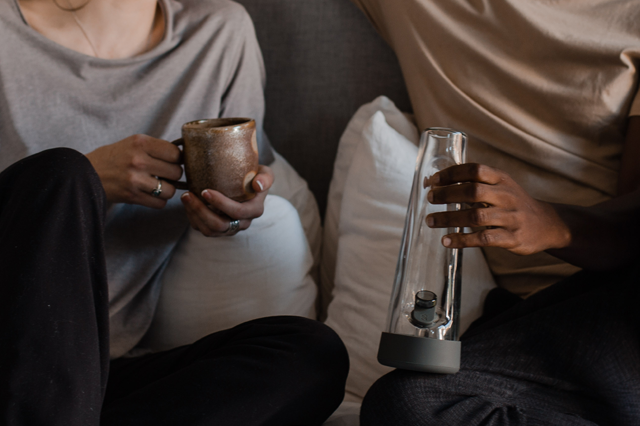 Two people relaxing on a couch with a ceramic mug and a clear Session bong, capturing a calm moment that introduces a guide to intentionally doing nothing.