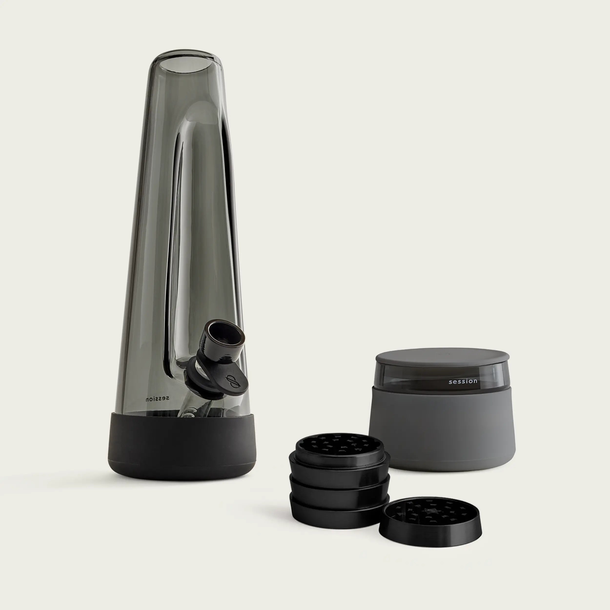 The Session Goods Starter Bundle, featuring a designer ash-colored glass bong with a black silicone base and downstem, a black metal grinder, and a  stash jar with a silicone smell proof lid, all set against a clean white background.