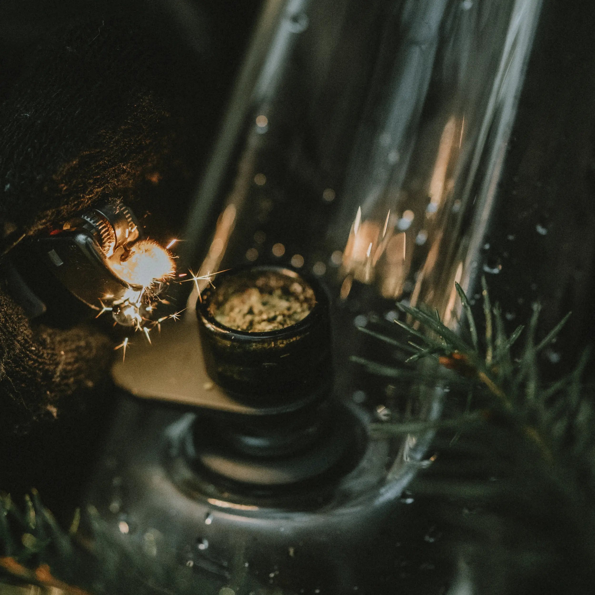 Close-up of a glass container with a lit candle inside, surrounded by greenery.