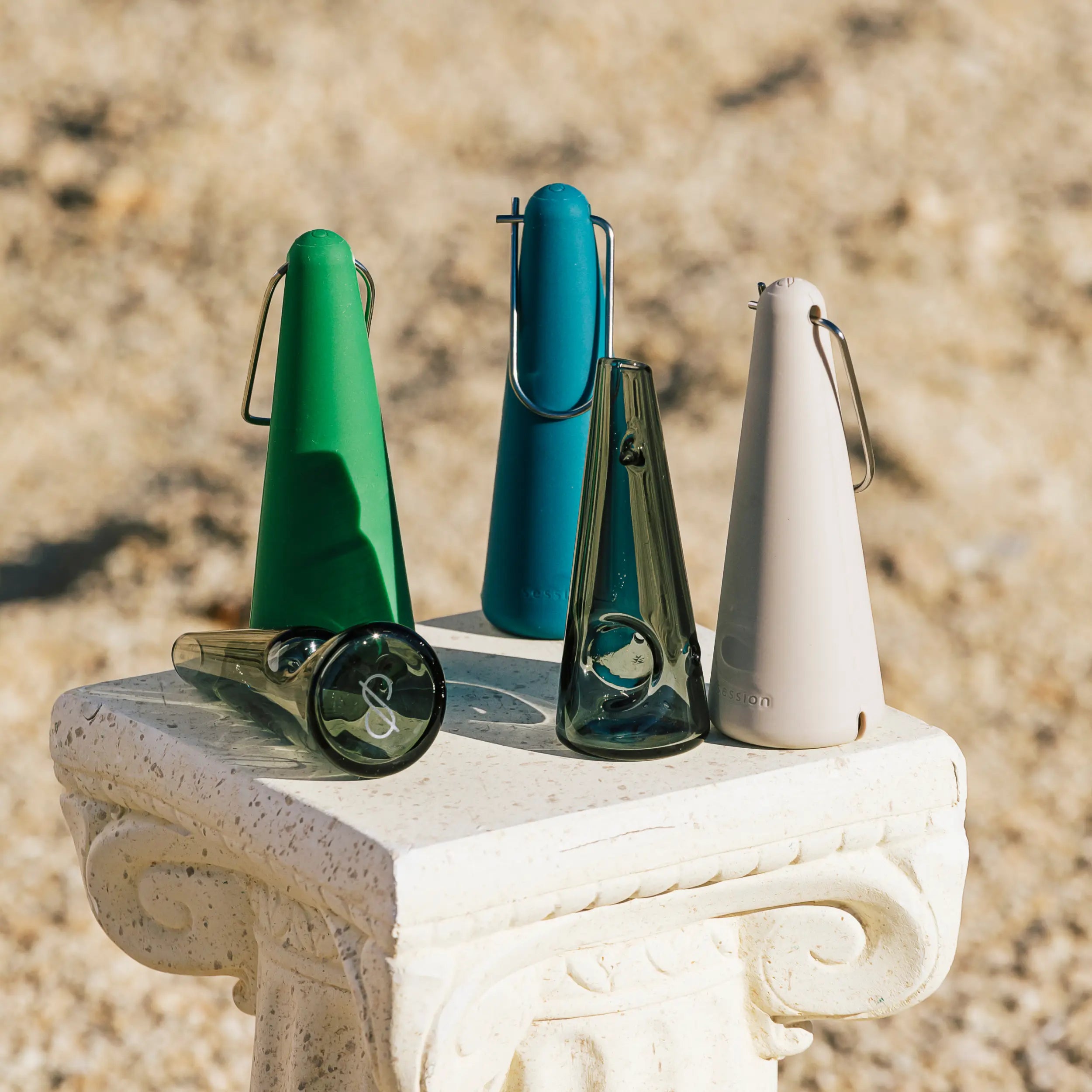 Session Goods portable glass pipes in limited edition green, teal, and cream silicone carry cases displayed on a white pedestal for the Winter Games collection.