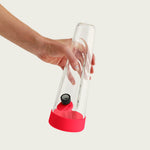 A hand holding a sleek Session Goods clear glass bong featuring a protective cherry red silicone base, an ergonomic indentation, and a matching bowl tab against a white studio background.