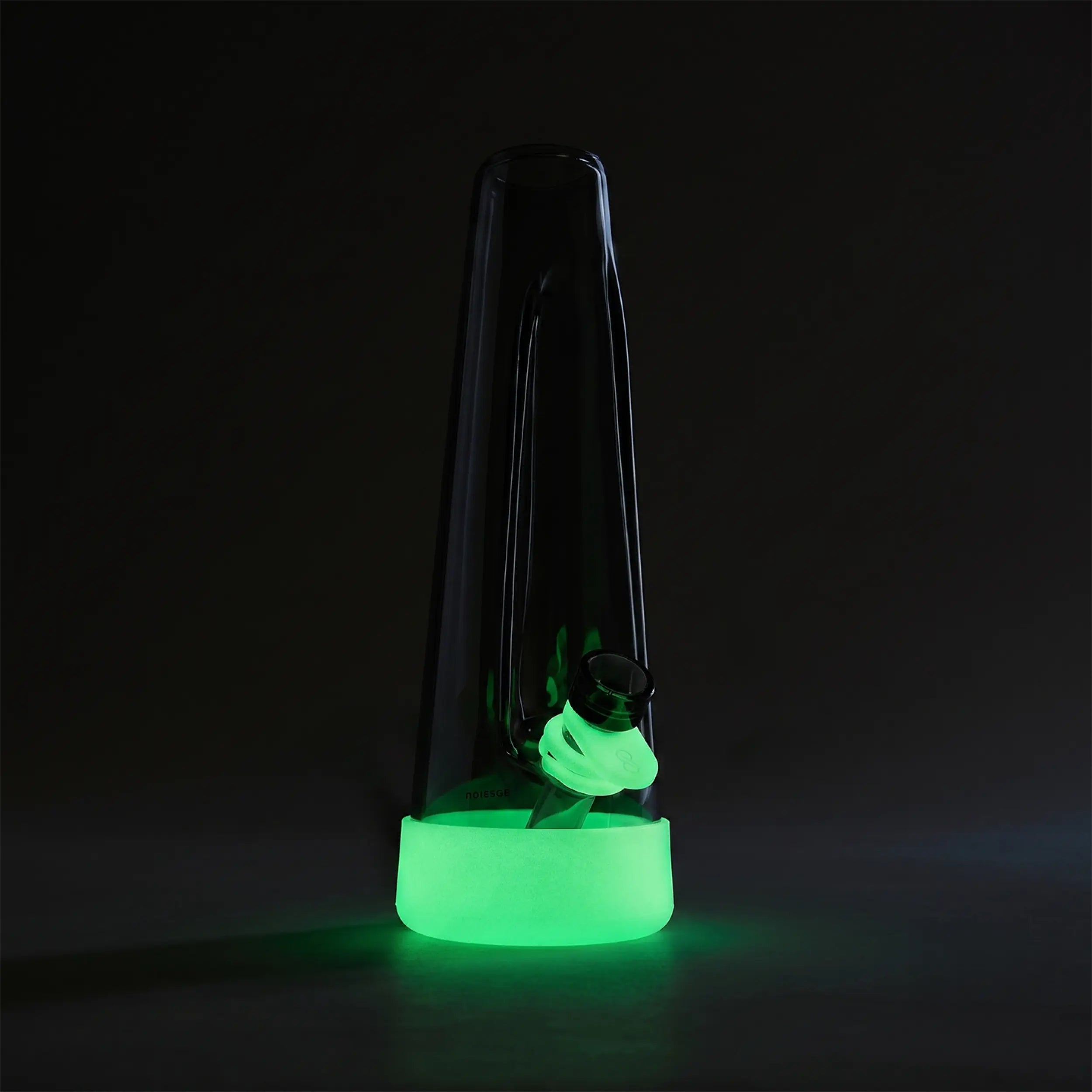 A conical dark glass water pipe with a mint green silicone base and bowl ring glowing brightly in a dark room.