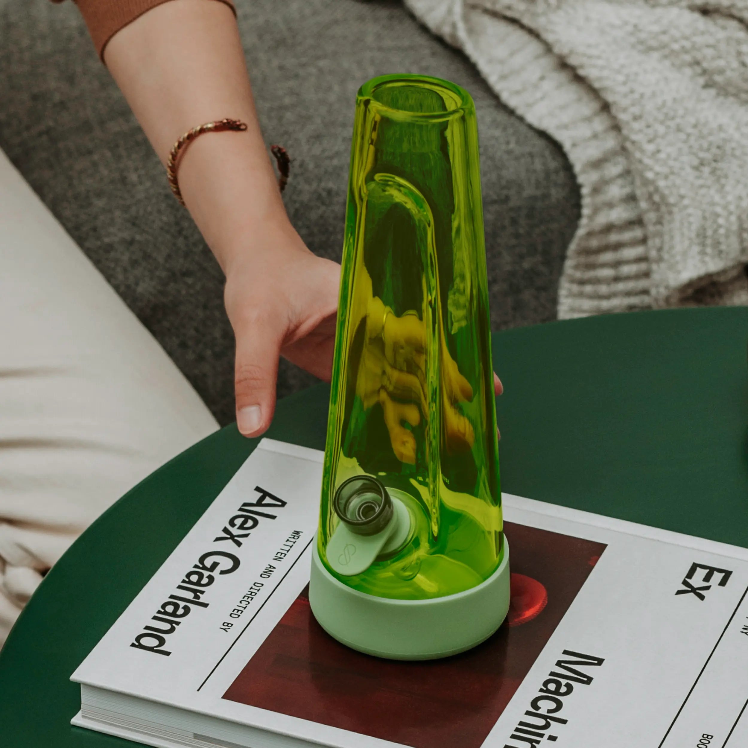 Hand reaching for Session Goods Grass Bong resting on a coffee table with a design book, showcasing modern form and functional style