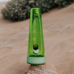 Session Goods Designer Series Grass Bong standing on sand with a blurred background, featuring sleek green glass and soft green silicone
