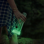 Person walking on an outdoor night trail holding the Session Goods glow-in-the-dark glass bong, featuring a luminescent lime green silicone base illuminating the dark.