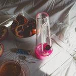 A high-end lifestyle shot of the Magenta Pink Session Bong on a breakfast tray, styled with fresh pomegranates, blood oranges, and a cup of tea for a curated home aesthetic.