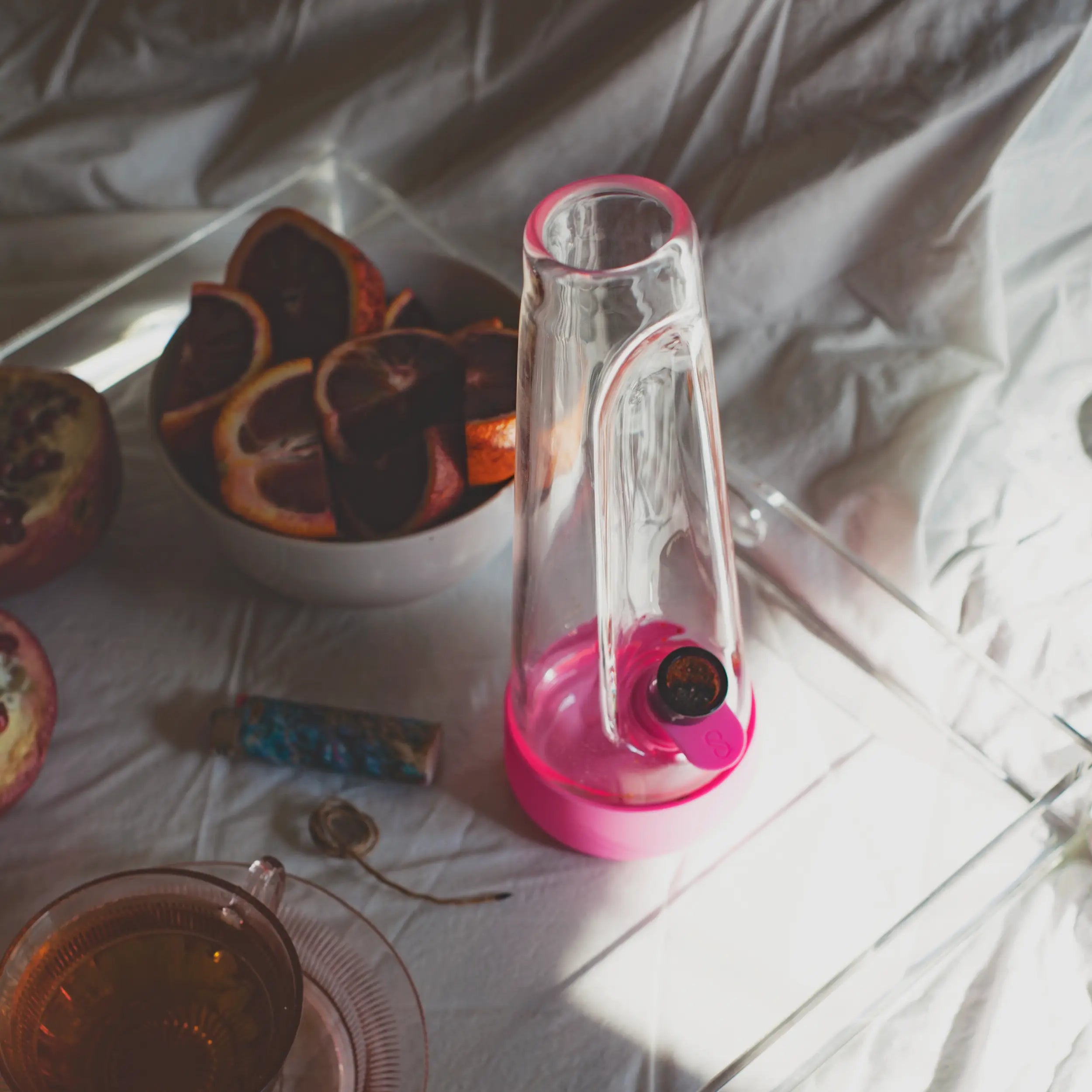 A high-end lifestyle shot of the Magenta Pink Session Bong on a breakfast tray, styled with fresh pomegranates, blood oranges, and a cup of tea for a curated home aesthetic.