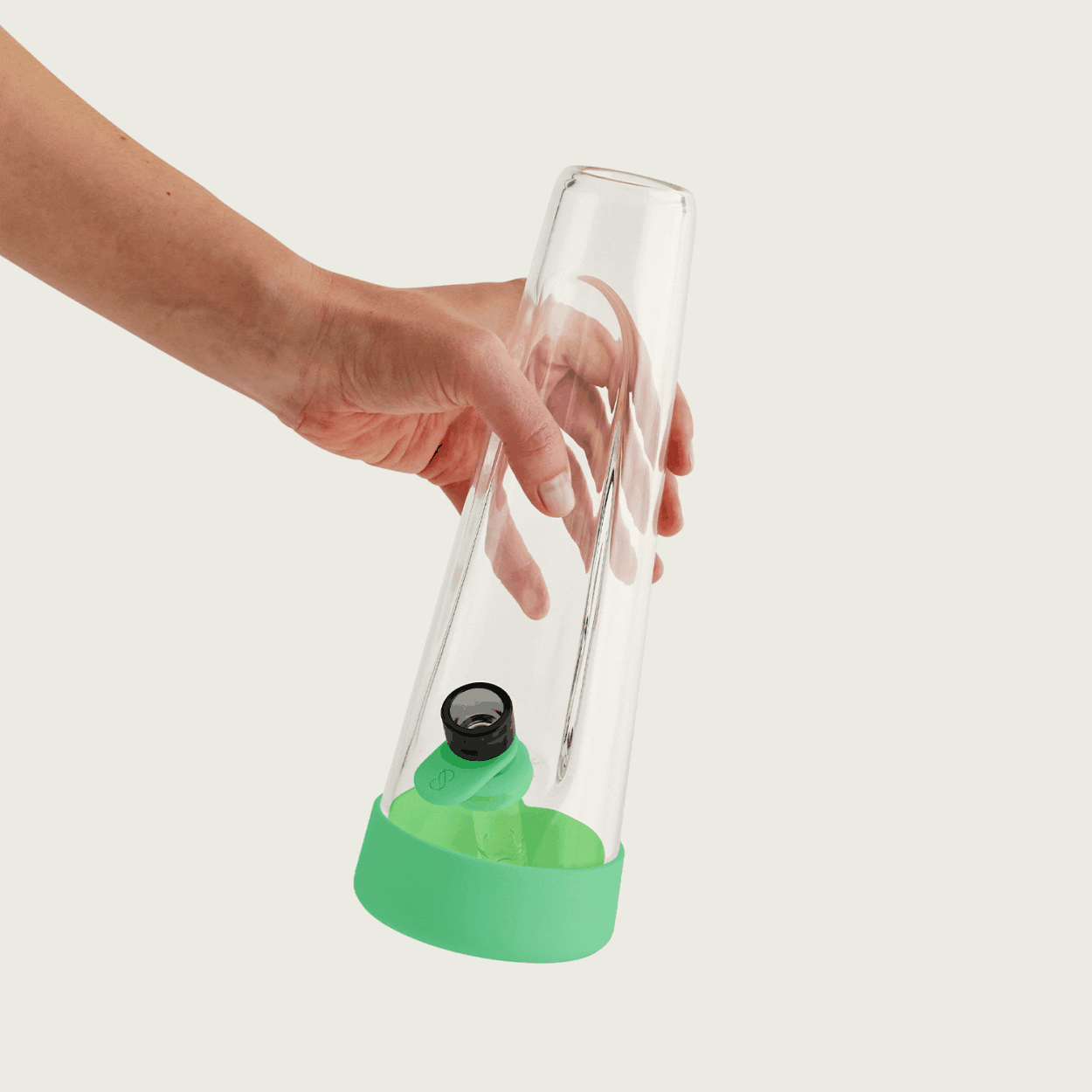 Close-up studio shot of a hand holding the Session Goods glow-in-the-dark water pipe, highlighting the brightly glowing lime green silicone base and bowl tab in a dark setting.