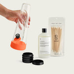 Vibrant Horizon Orange Session Goods starter bundle featuring an orange-accented glass bong and a four-piece metal grinder on a light wood table.