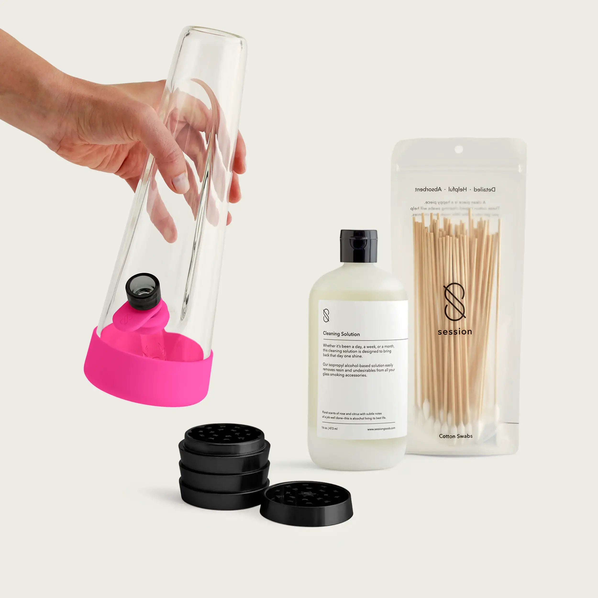 A hand holds the architectural glass Session Bong fitted with Magenta Pink silicone accessories, displayed with the core starter trio of an industrial-grade grinder, cleaning solution, and cotton swabs.