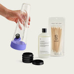 A Moonlight Purple Session Goods starter set with a purple-wrapped glass water pipe and metal grinder, highlighting its soft, architectural design.