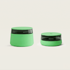 A side-by-side studio shot of the Session Goods glow-in-the-dark lime green bundle on a white background, featuring the tall glass and silicone Stash Jar on the left next to the matching low-profile Ashtray on the right.
