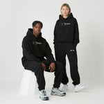 Two people wearing black hoodies and pants with a Normform logo on a white background