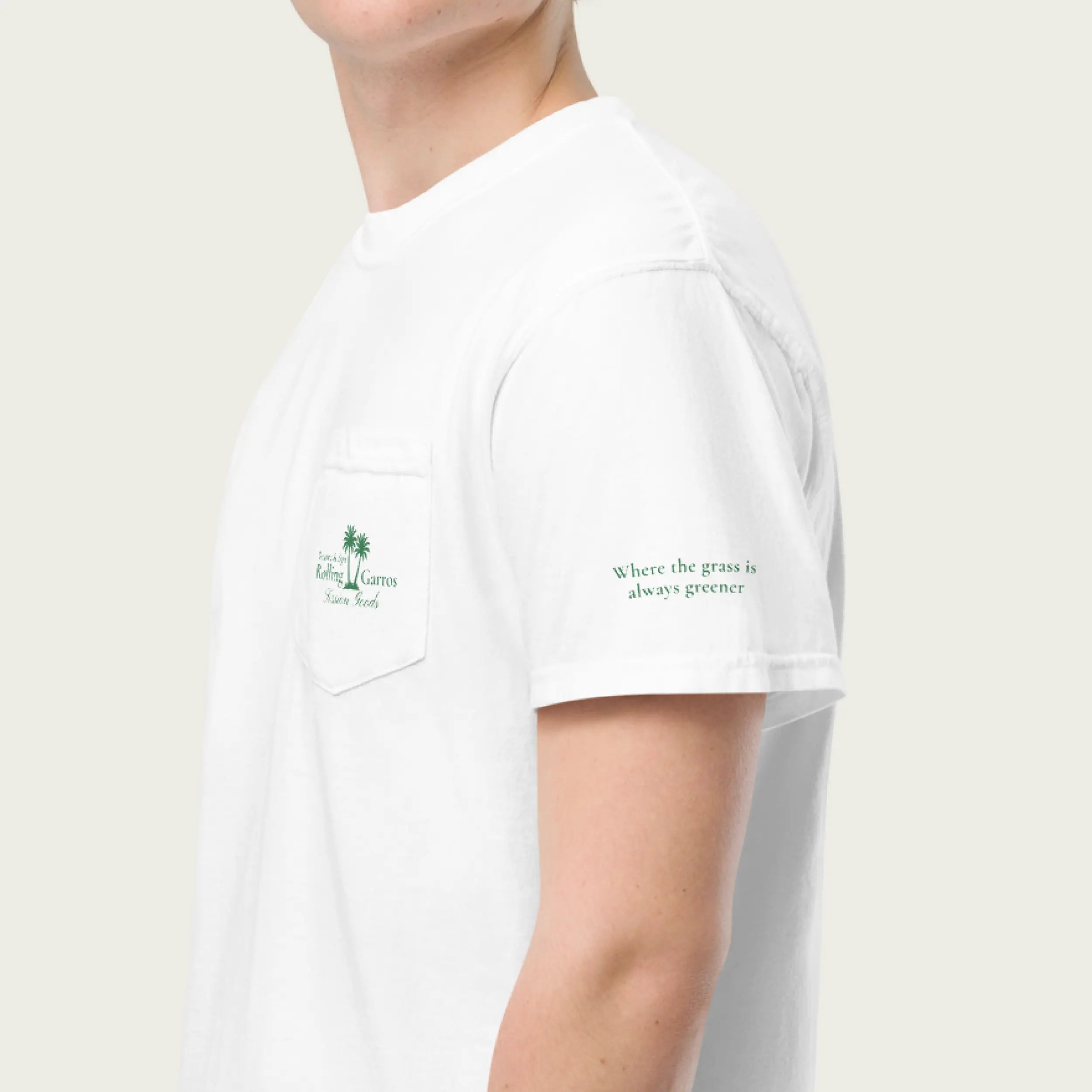 Close-up side view of white Session Goods Rolling Garros club t-shirt with green palm tree pocket logo and sleeve text ‘Where the grass is always greener.’