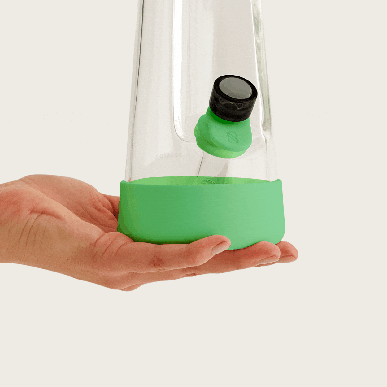 A close-up of a clear glass water pipe with a glow lime green silicone base protector, being held by a person's hand. The water pipe is filled with water and has a black-rimmed bowl and downstem, all against a plain white background.