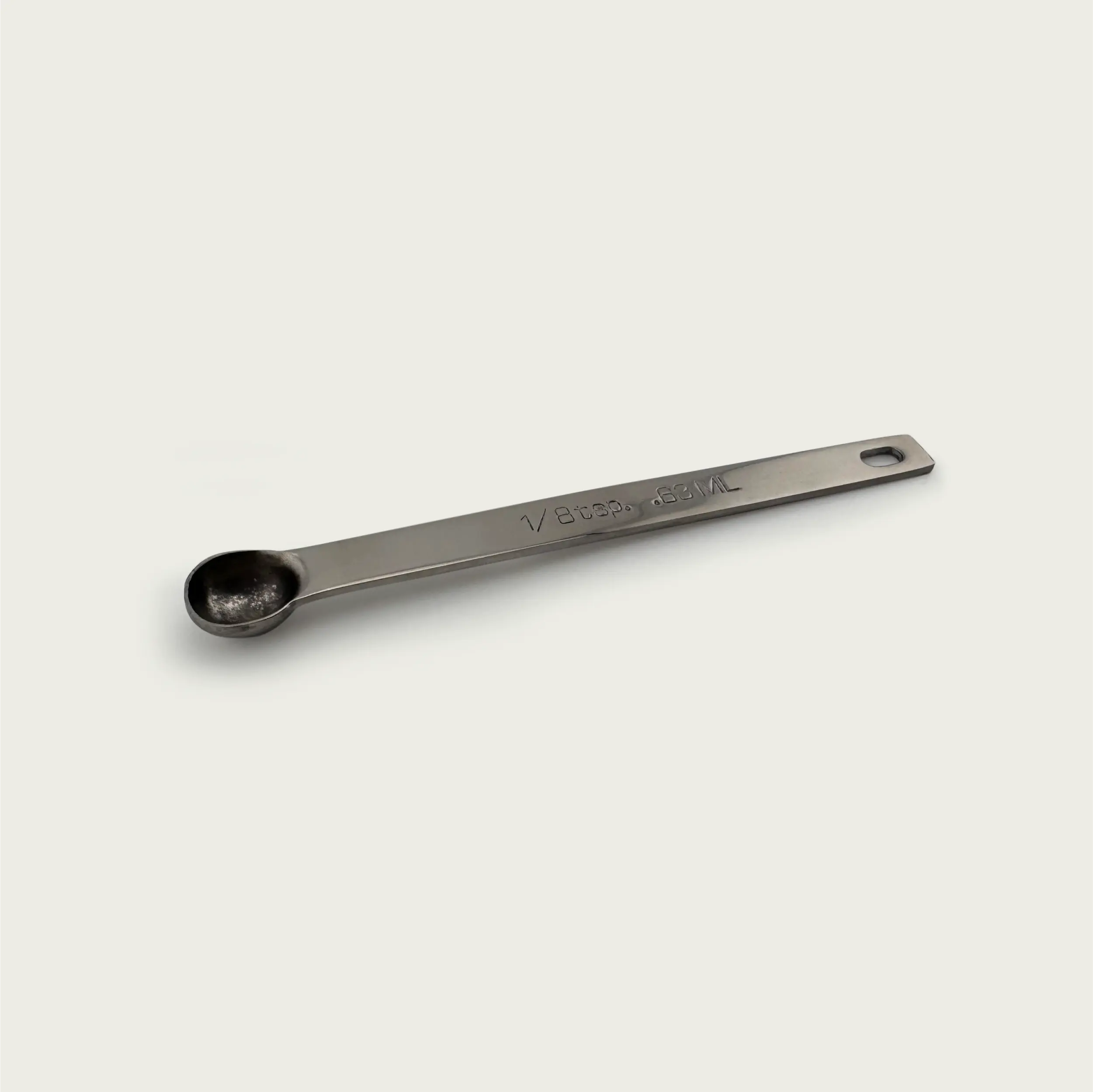 Stainless steel 1/8 teaspoon measuring spoon with engraved 0.63 mL marking, shown at an angled side perspective on a light background.