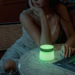 A woman sits at a marble table in a dimly lit room next to a fully illuminated, glow-in-the-dark lime green Session Goods stash jar and ashtray.