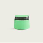 The Session Goods lime green stash jar and ashtray fully illuminated in a dark studio, showcasing its bright glow-in-the-dark silicone body and lid against a black background.