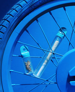 dream color-ways stash pod and stash tube by session goods, displayed between bike spokes. Stash tube is holding a pre-roll, and stash pod is holding flower